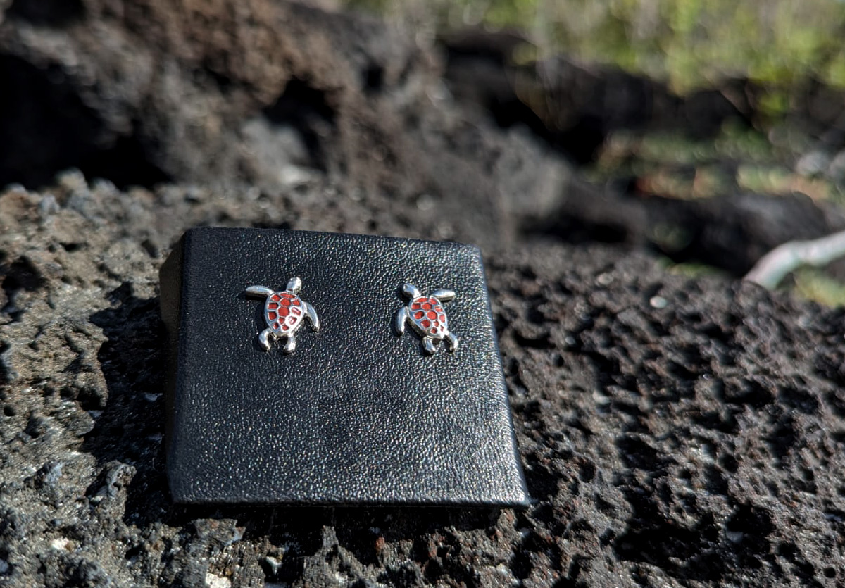 Red and silver sea turtle earrings on lava rock